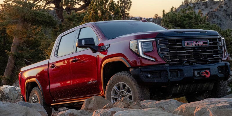 2026 GMC Sierra 1500 driving up rocks in Garden City Park, NY, showcasing its off-road capability with the AT4 trim's lifted suspension and all-terrain tires.